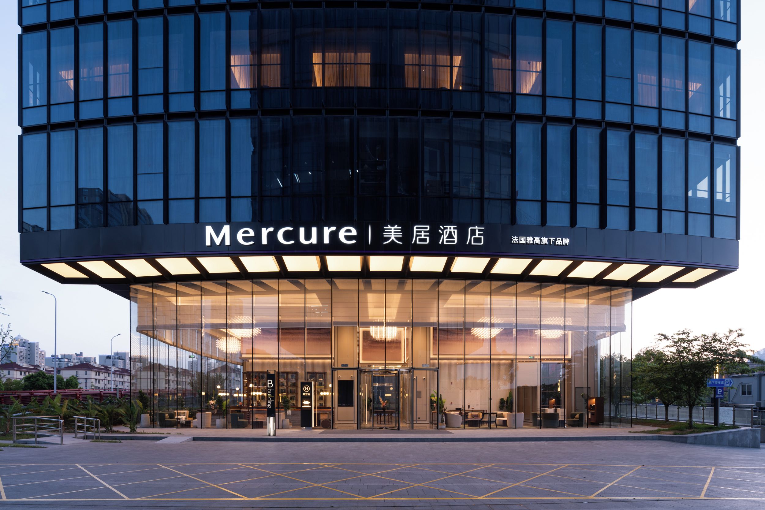 A modern hotel with a glass facade, a prominent entrance, and outdoor seating areas.