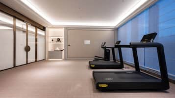 Un gimnasio con cintas de correr, dispensador de agua y una pequeña zona de estar con un reloj y objetos decorativos.