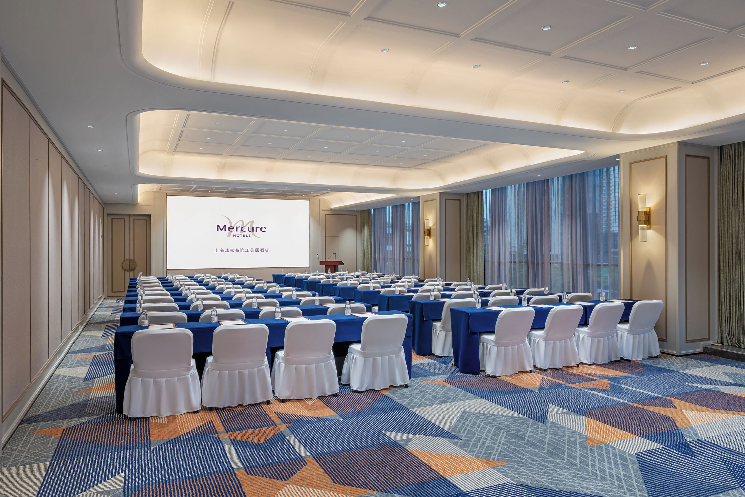 A conference room with rows of tables and chairs, a projection screen, and a podium.