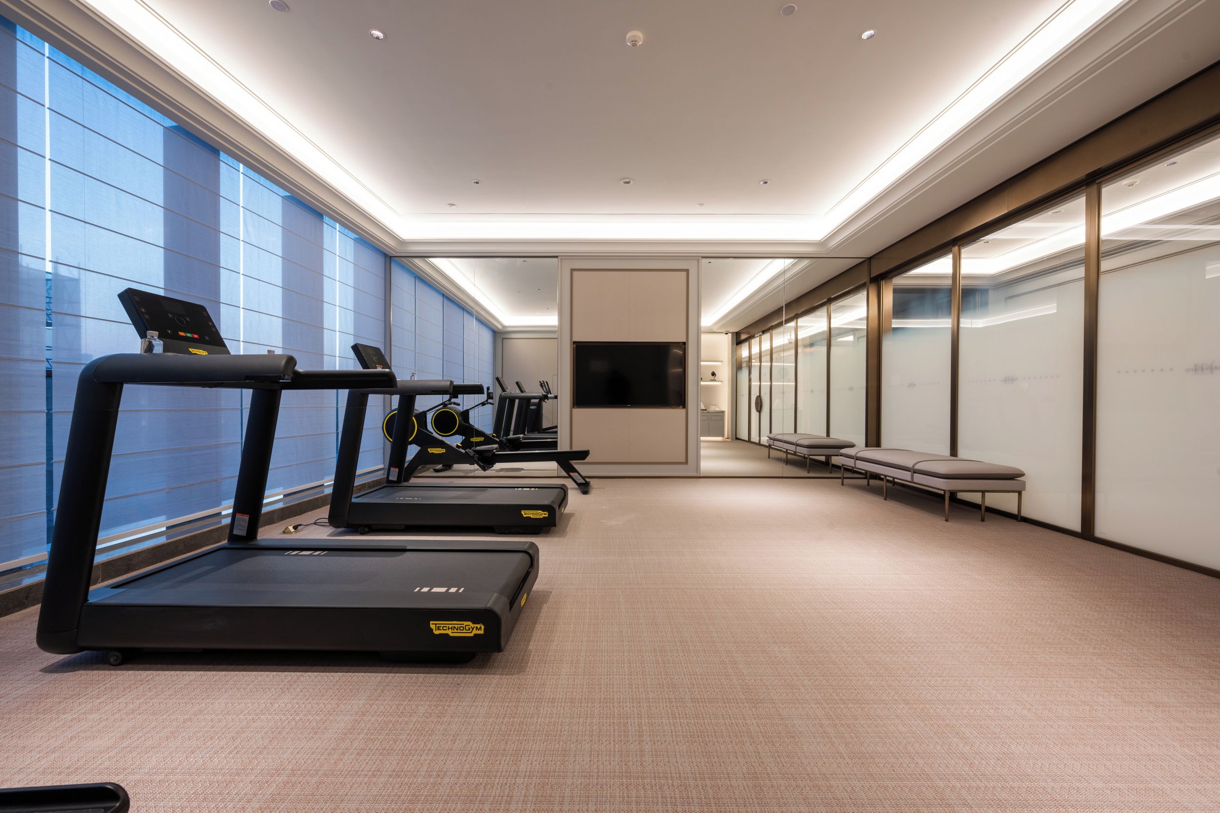 A modern gym with treadmills, a bench, and a TV screen.