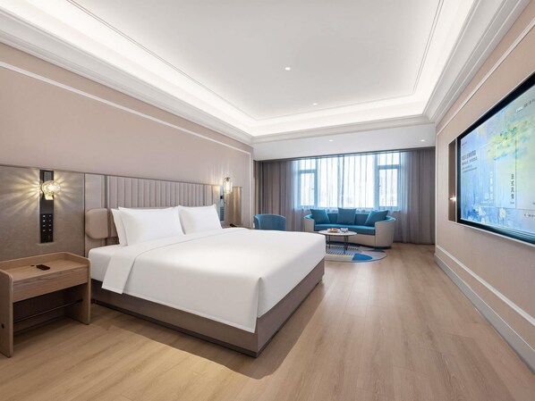 A modern hotel room with a large bed, a desk, a sofa, and a TV screen displaying a map.