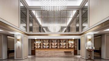 A spacious lobby with a marble reception desk, a large chandelier, and a high ceiling with skylights.