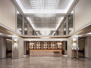 A spacious lobby with a marble reception desk, a large chandelier, and a high ceiling with skylights.