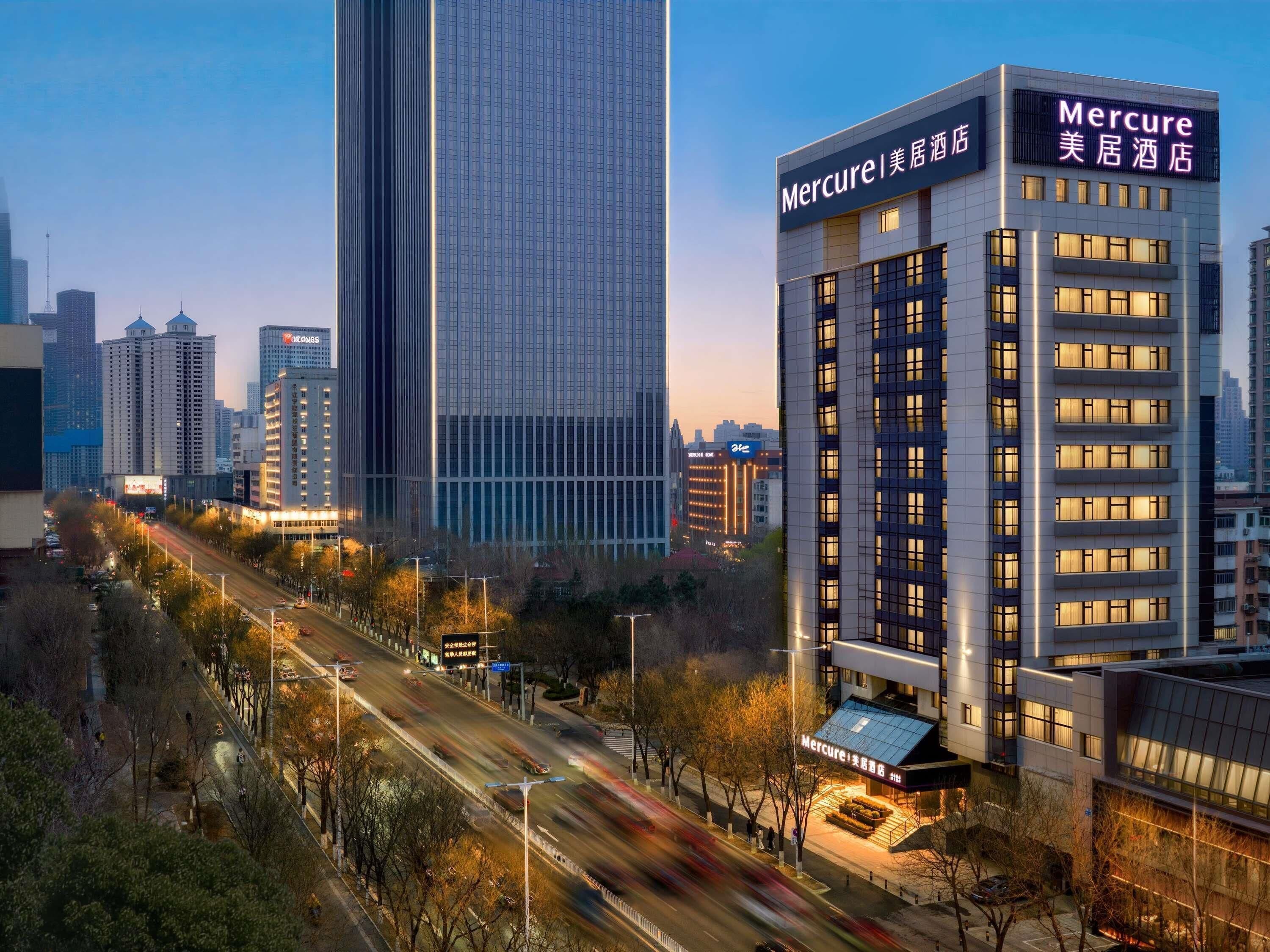 A modern hotel with a prominent sign, surrounded by high-rise buildings and a busy street.