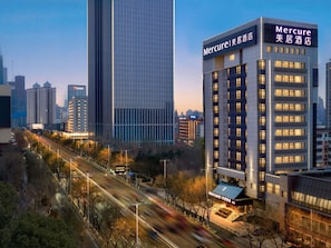 A modern hotel with a prominent sign, surrounded by high-rise buildings and a busy street.