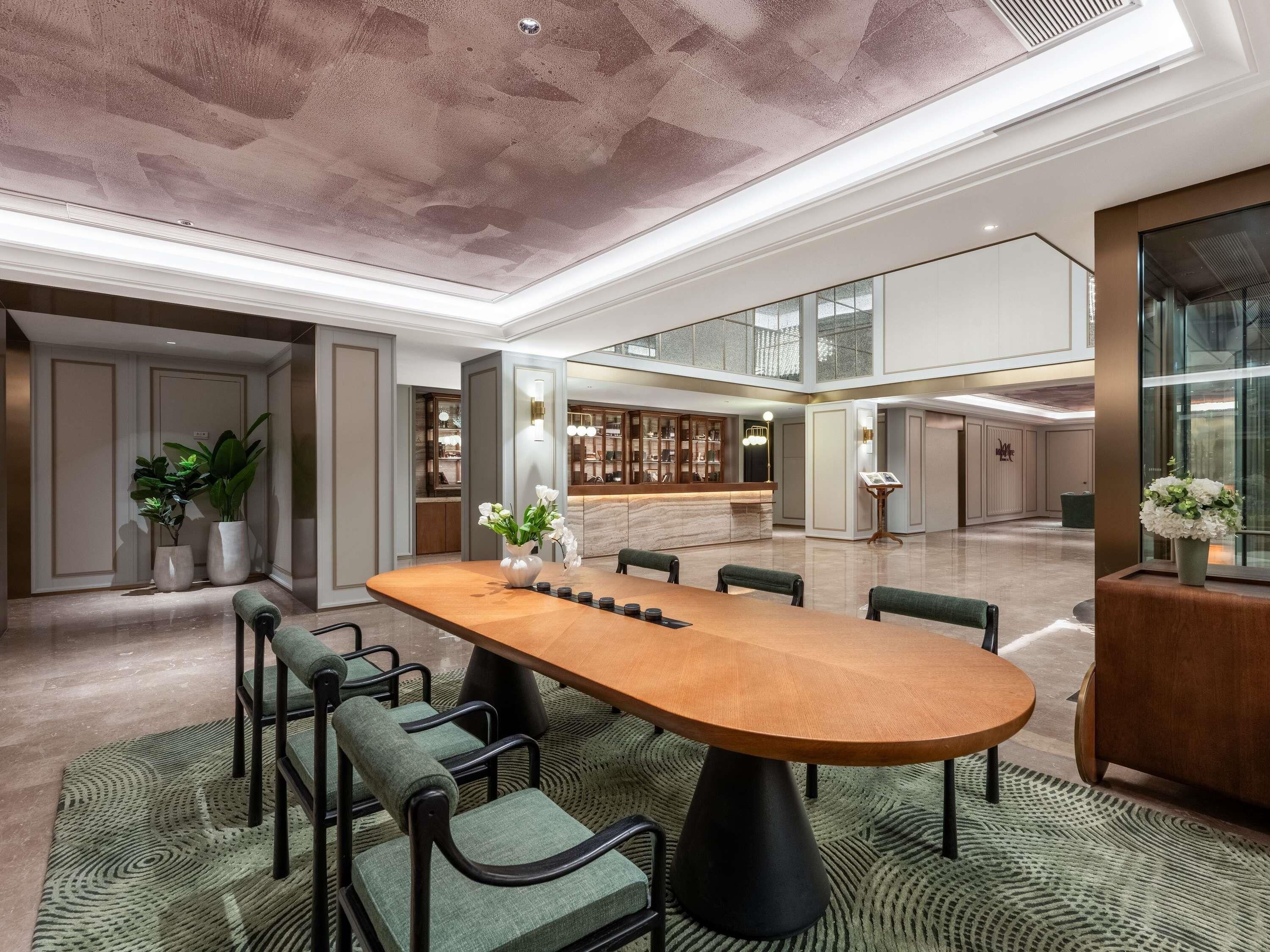 Un vestíbulo amplio con una mesa de madera central, asientos y una zona de bar.