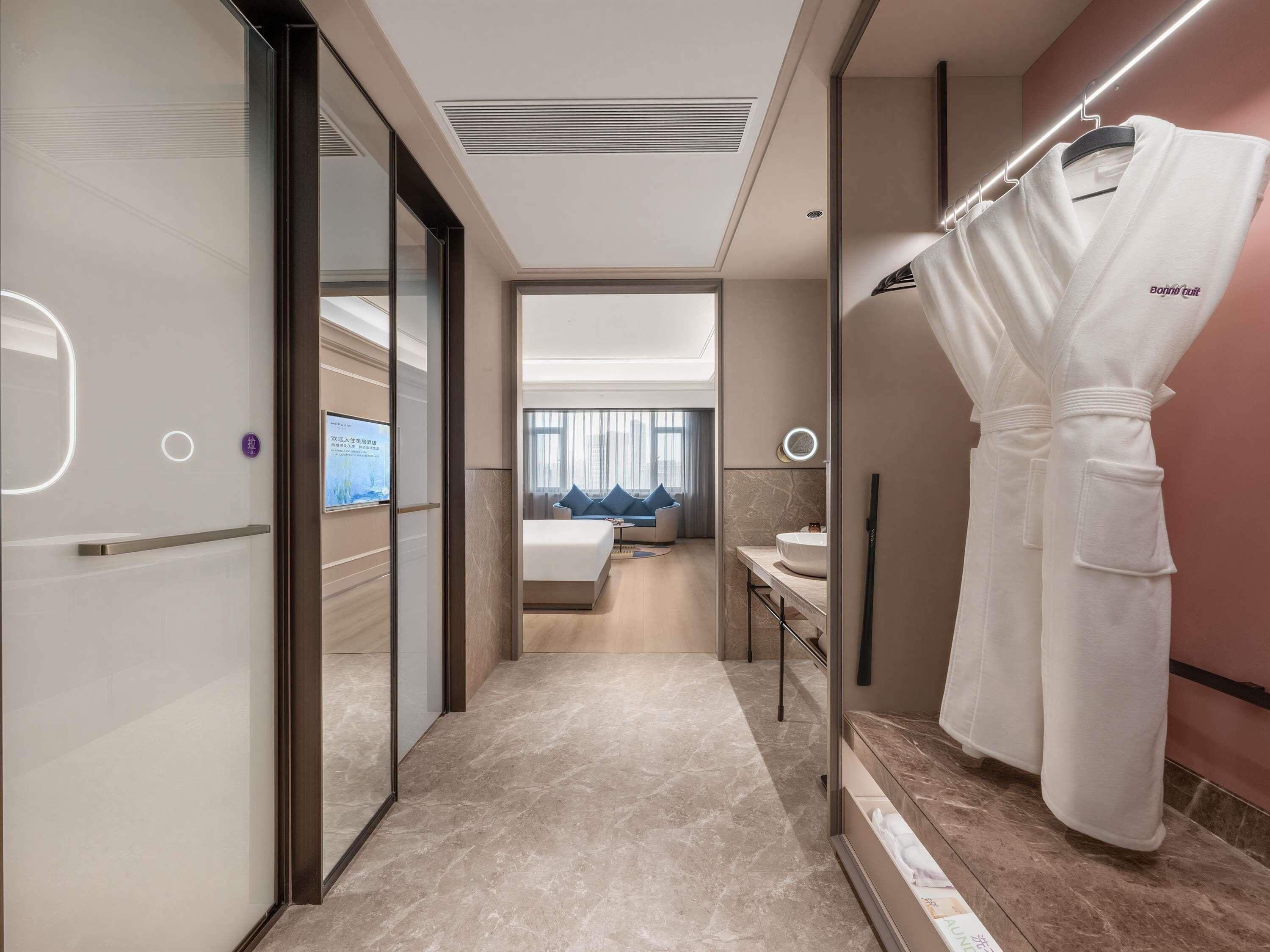 Habitación de hotel con cama, baño con lavamanos y bata colgada en un perchero.