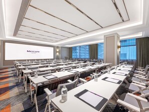 Ein Konferenzraum mit Tischen, Stühlen und einer großen Leinwand, auf der 'Mercure Hotels' angezeigt wird.