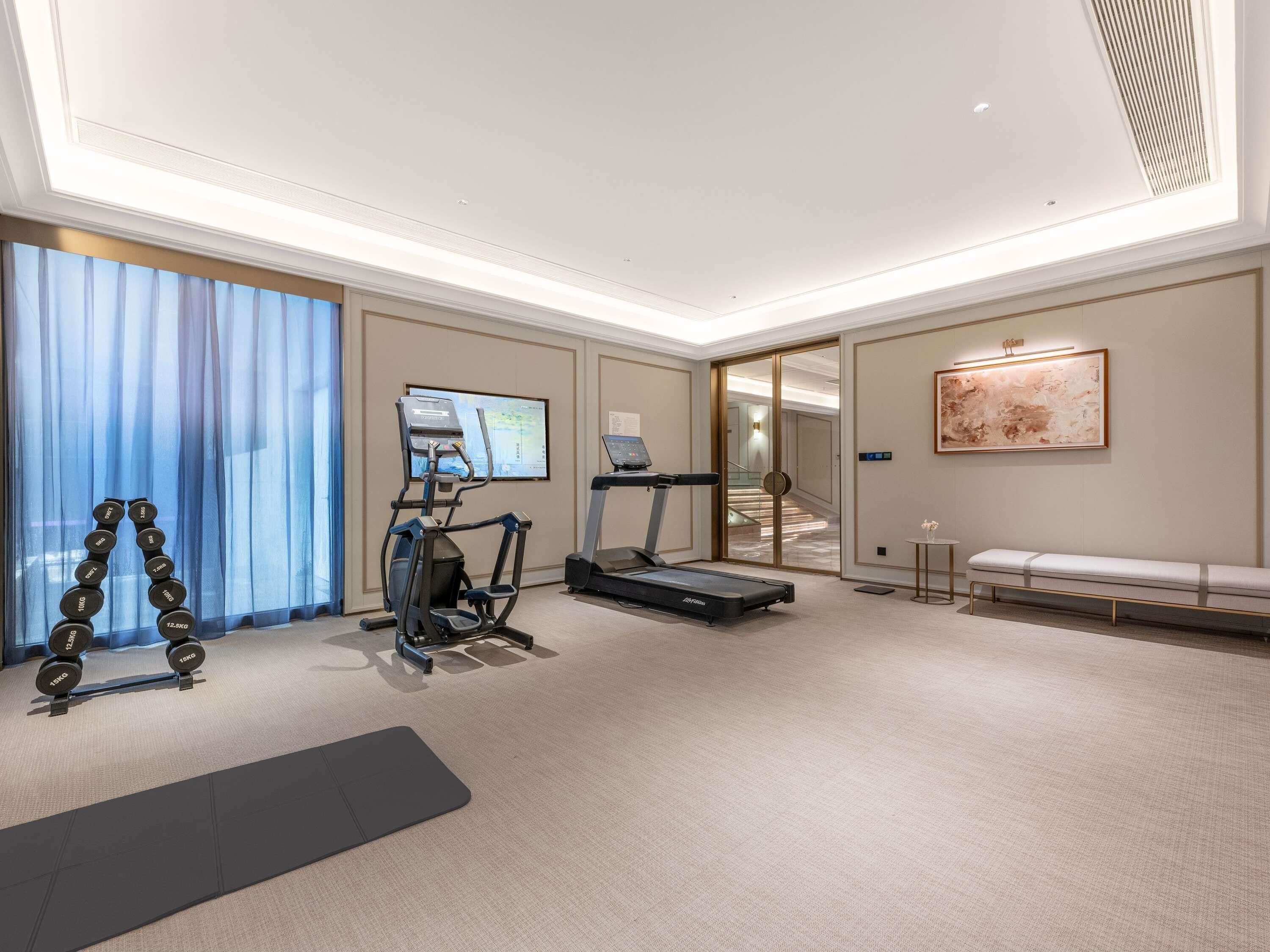 A fitness room with a treadmill, elliptical, and dumbbells.