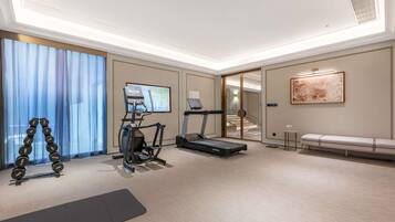 A fitness room with a treadmill, elliptical, and dumbbells.
