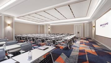 A conference room with rows of tables and chairs, a patterned carpet, and a large screen displaying 'Mercure Hotels'.