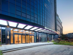 Une entrée d’hôtel moderne avec une façade en verre, un espace d’entrée abrité et une enseigne indiquant « Mercure ».
