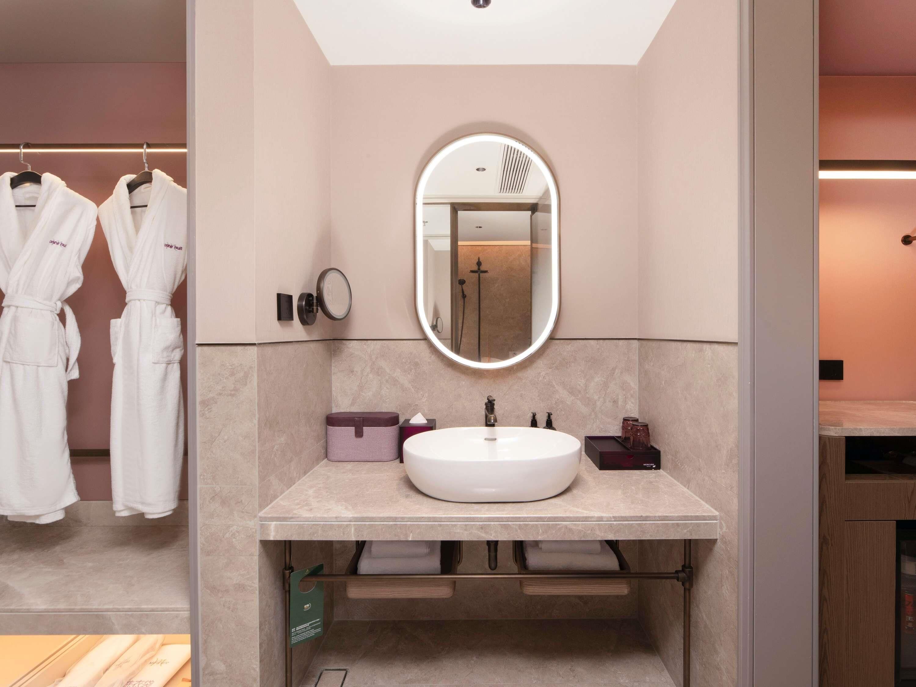 A modern bathroom with a large mirror, a white sink, and a robe rack.
