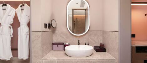 A modern bathroom with a large mirror, a white sink, and a robe rack.