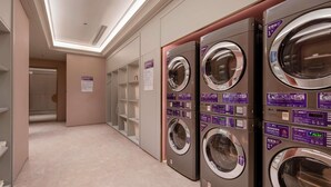 Fila de lavadoras empotradas con paneles de control, piso de baldosas y una puerta que da a otra habitación.