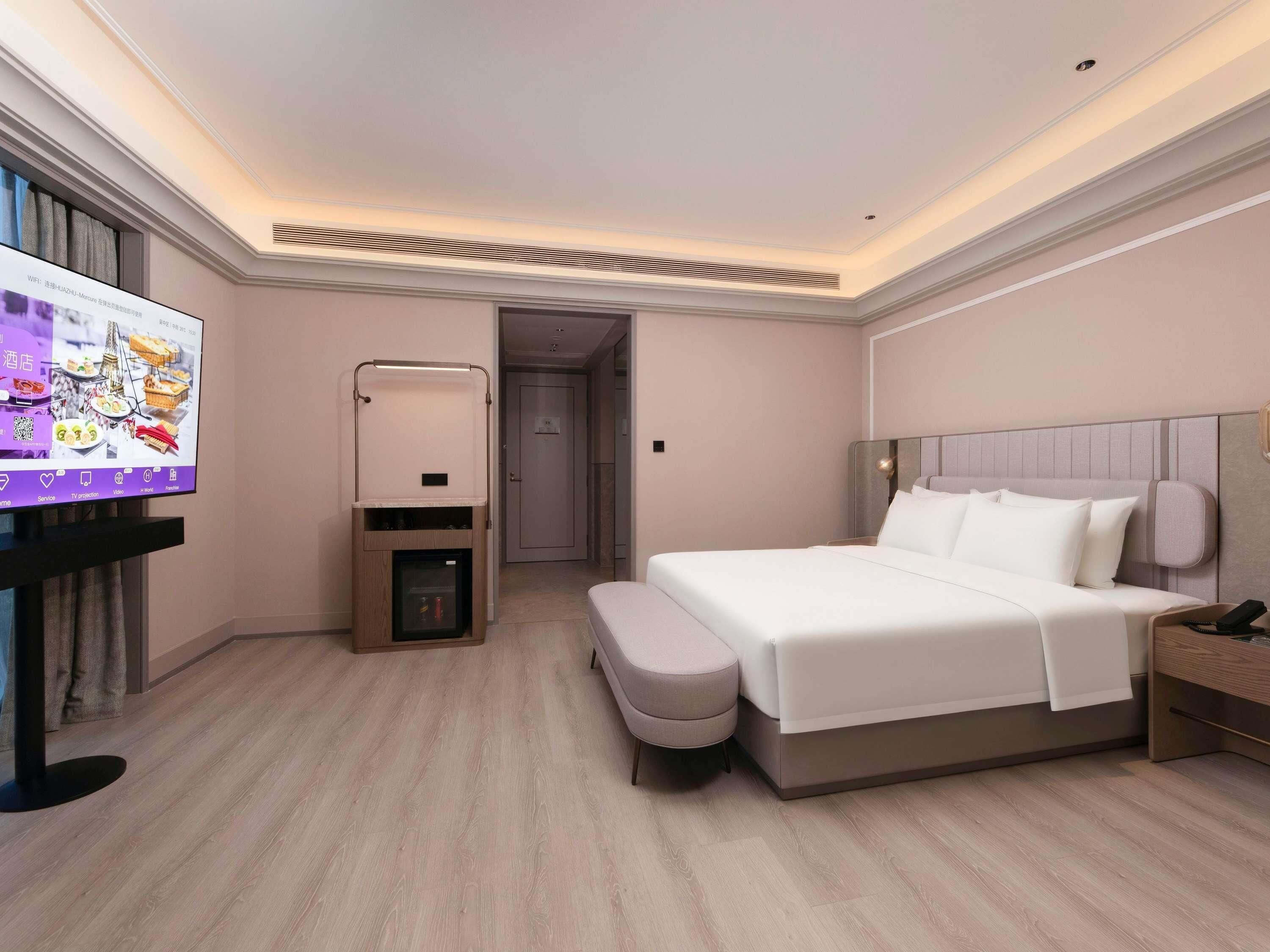 A hotel room with a bed, bedside table, TV, and a minibar.