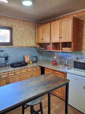 Una cocina con armarios de madera, una encimera, un fregadero, un microondas y un refrigerador pequeño.
