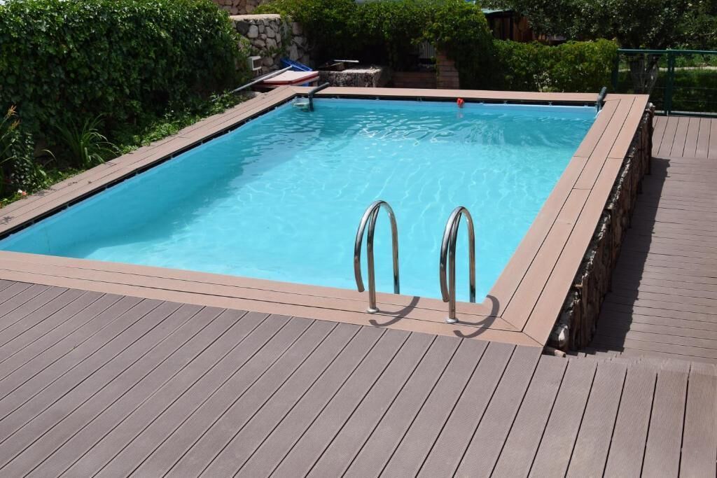 Una piscina rectangular con escaleras metálicas en un lateral, rodeada por una terraza de madera.