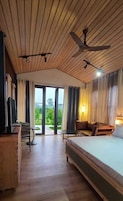 Quarto de hotel com cama, escrivaninha, cadeira, luminária e ventilador de teto.