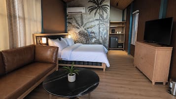 Habitación de hotel con cama, sofá, una mesita con una planta, televisor y armario.