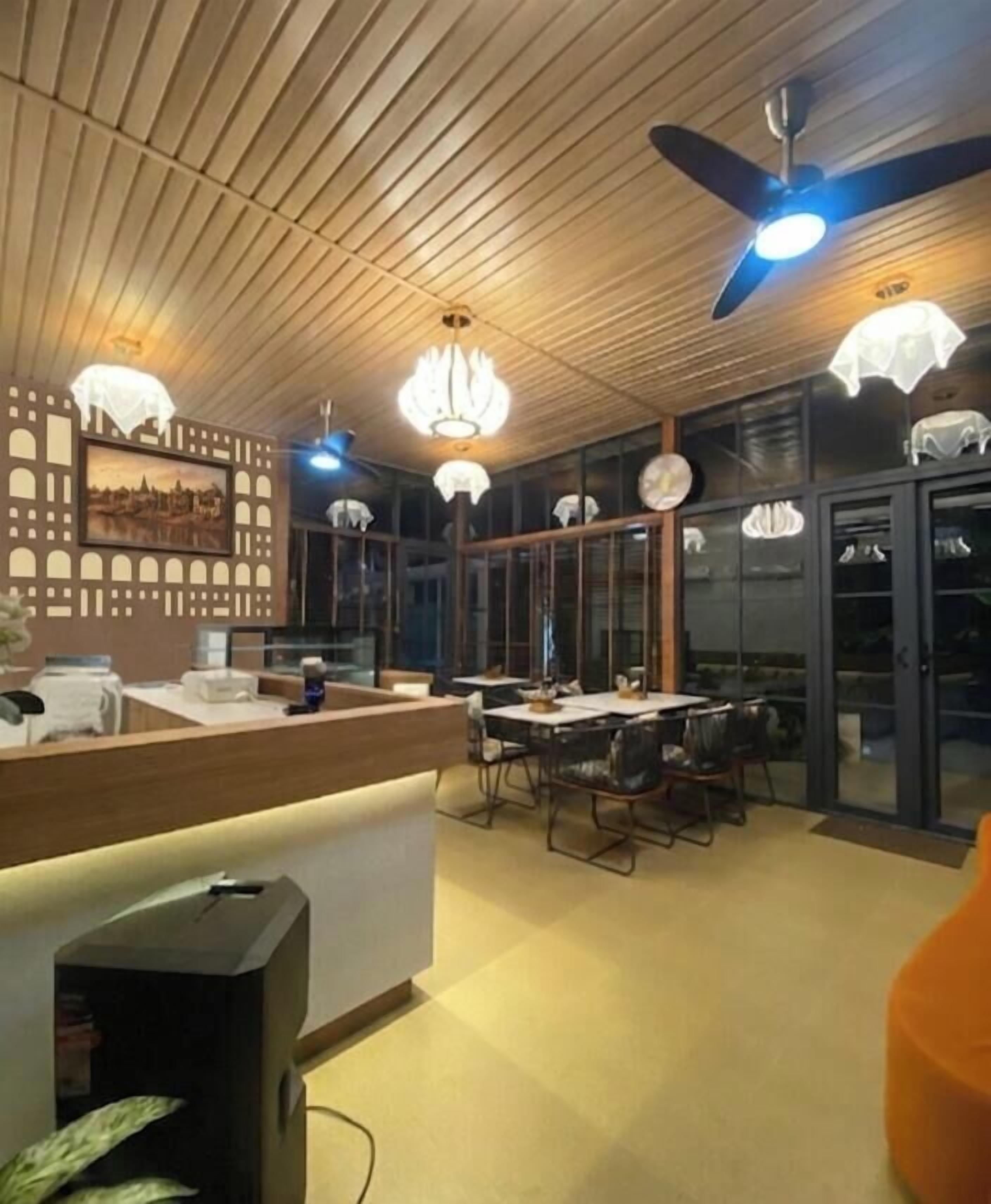A modern interior with a wooden ceiling, a reception desk, dining area with chairs, and pendant lighting.