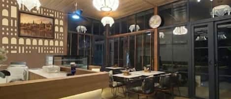 Un interior moderno con techo de madera, mostrador de recepción, zona de comedor con sillas e iluminación colgante.