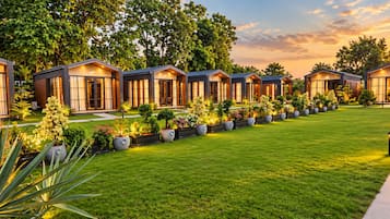 A row of modern, well-lit cabins with a neatly maintained lawn and potted plants in front.