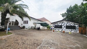 A courtyard with a paved walkway, a white building with a red roof, and a mural on the adjacent wall. -  1-BR Bright & Quite Apartment & Large Living Room (Accra)