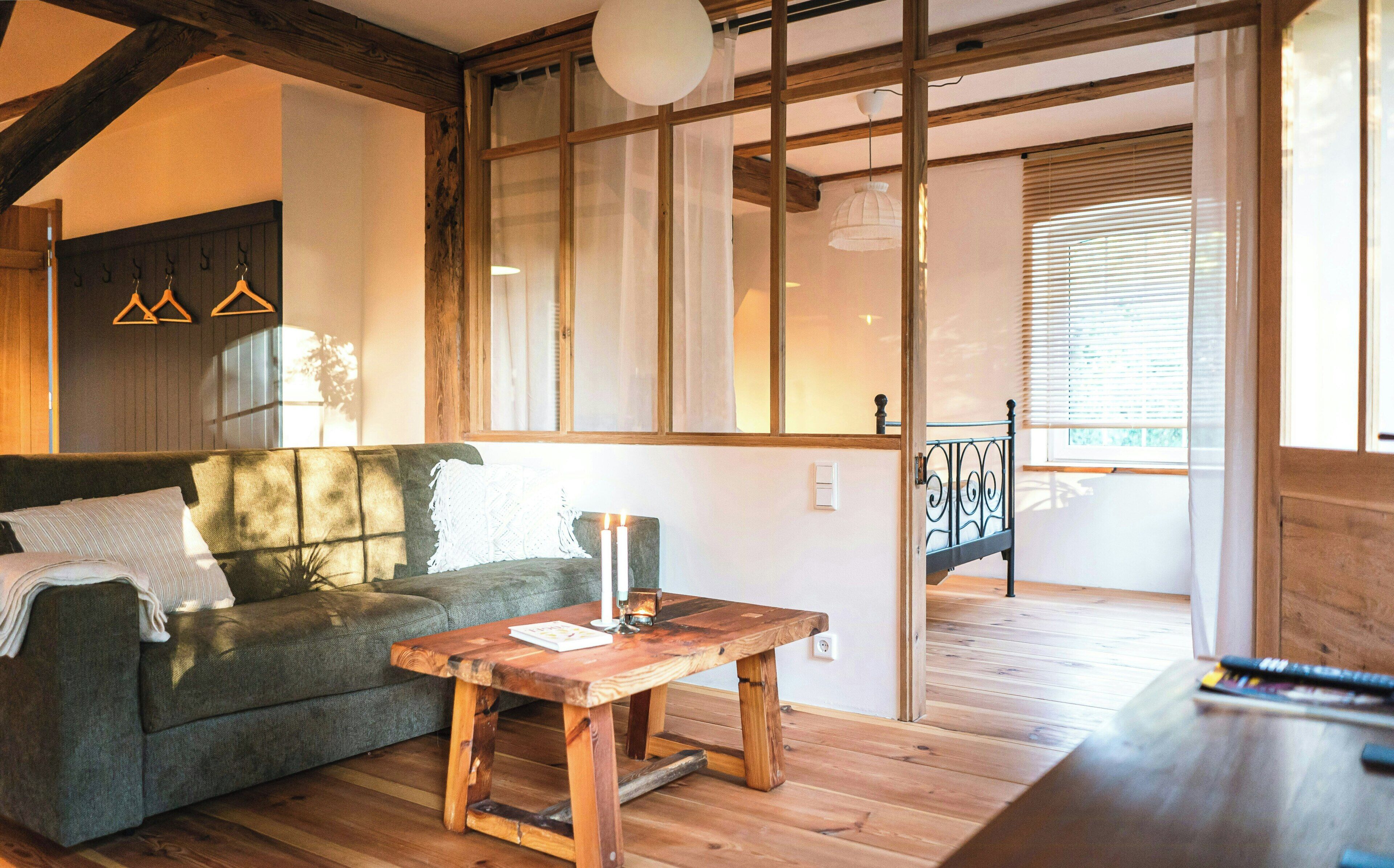 Ein gemütliches Wohnzimmer mit einer Couch, einem Holztisch und Blick auf einen Balkon durch ein großes Fenster.