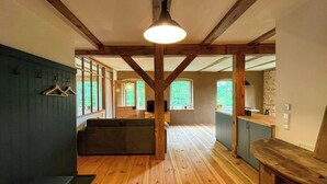 A spacious room with wooden floors, a sofa, a dining area with a table, and large windows allowing natural light.