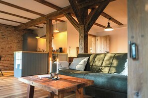 A cozy living room with a wooden table, a green sofa, and a brick wall.