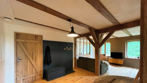 A room with wooden beams, a sofa, a television, and a large window.
