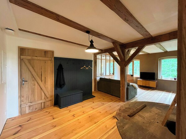 A room with wooden beams, a sofa, a television, and a large window.