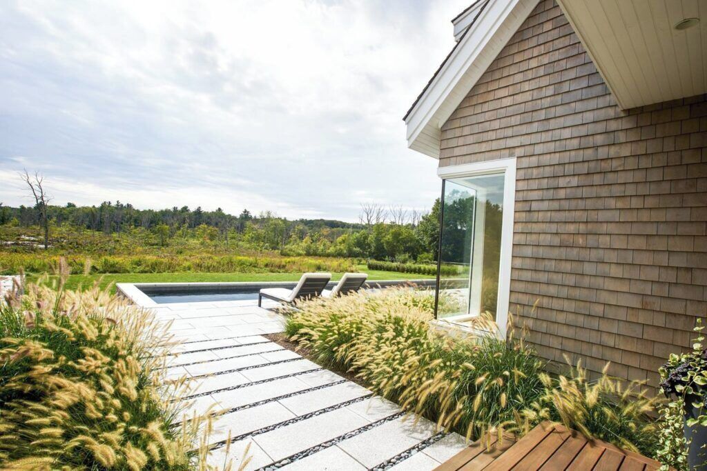 A modern house with a brick exterior, a glass door, and a patio with a pool and lounge chairs.