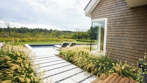 A modern house with a brick exterior, a glass door, and a patio with a pool and lounge chairs.