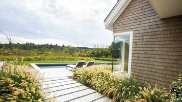 A modern house with a brick exterior, a glass door, and a patio with a pool and lounge chairs.