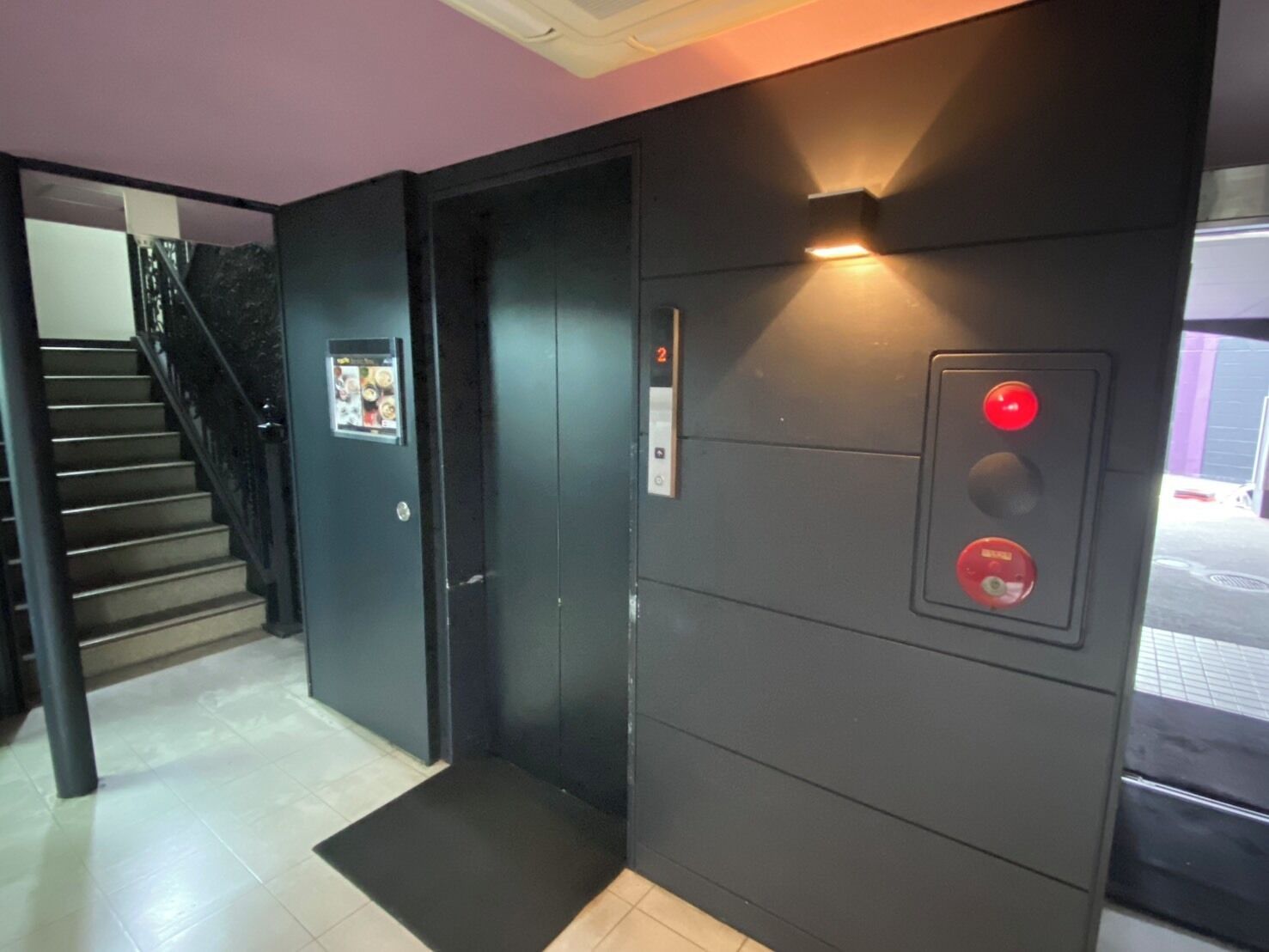 An elevator with a control panel and a door, a staircase with a handrail, and a tiled floor.