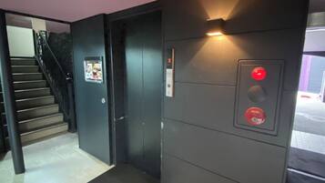 An elevator with a control panel and a door, a staircase with a handrail, and a tiled floor.