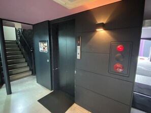 Um elevador com painel de controle e porta, uma escada com corrimão e piso revestido de azulejos.