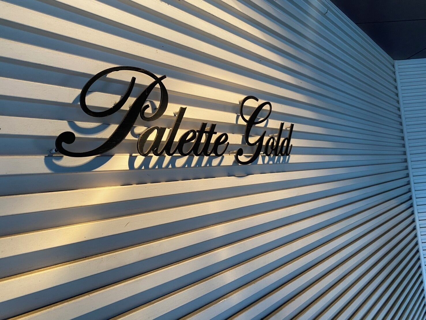 Uma placa de metal com as palavras 'Palette Gold' sobre um fundo branco com linhas horizontais.