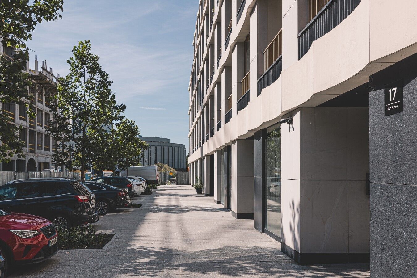 Ein modernes Gebäude mit schlichter Fassade, ein Parkplatz mit mehreren Autos und ein klarer Himmel.