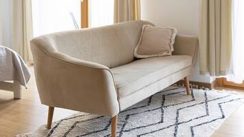 Ein beiges Sofa mit Holzbeinen, ein passendes Kissen und ein gemustertes Teppich auf Holzdielen.