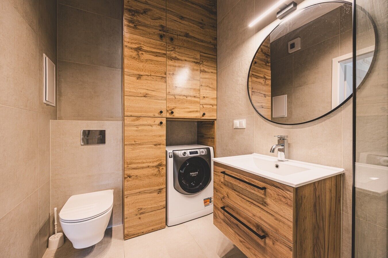 Une salle de bain moderne équipée de toilettes, d’un lave-linge et d’un meuble-lavabo en bois avec un miroir.