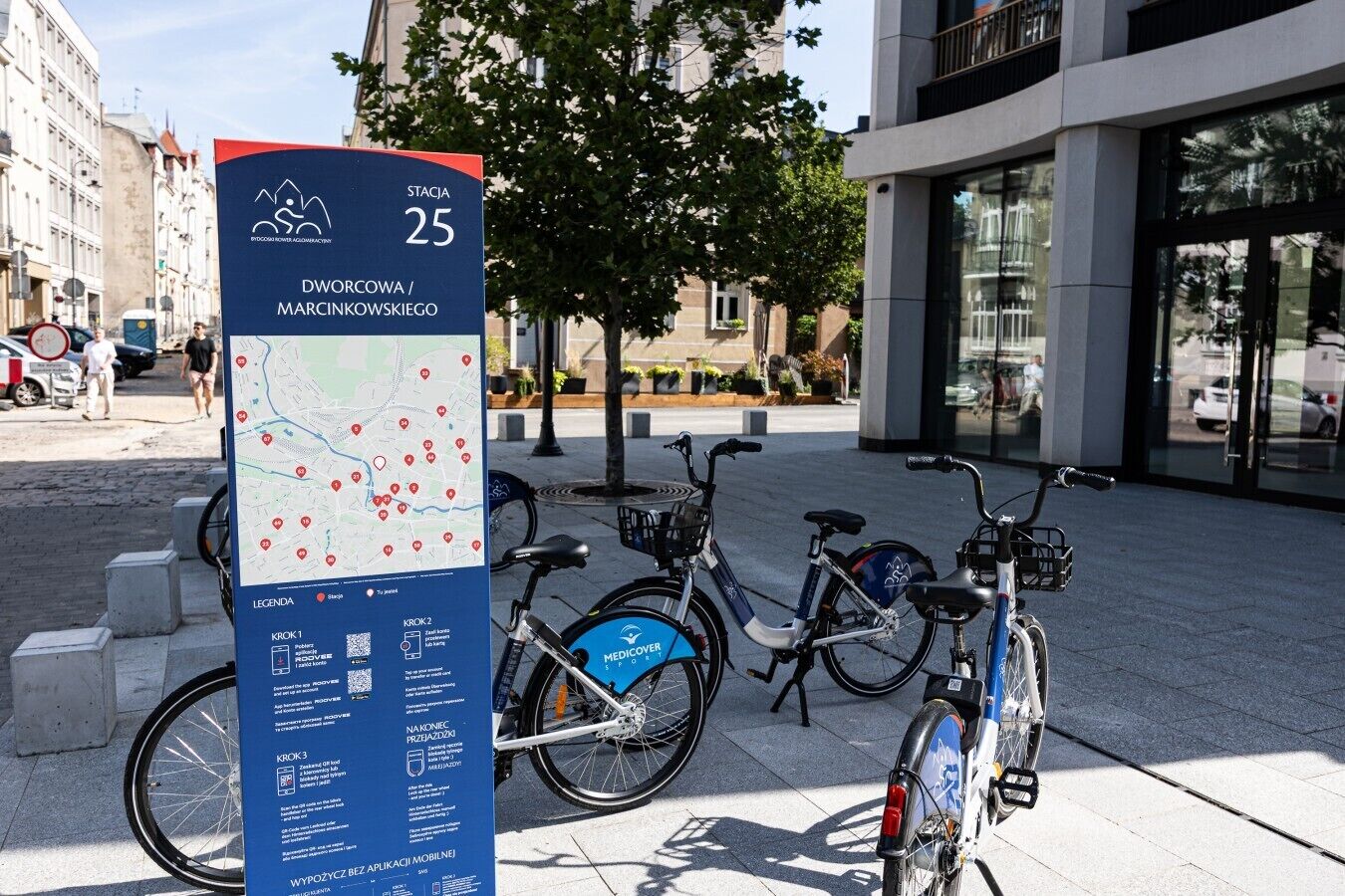 A map and bike rental station in an urban setting with buildings and trees.