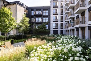 Un edificio residencial moderno con balcones, un jardín de flores blancas y un camino.