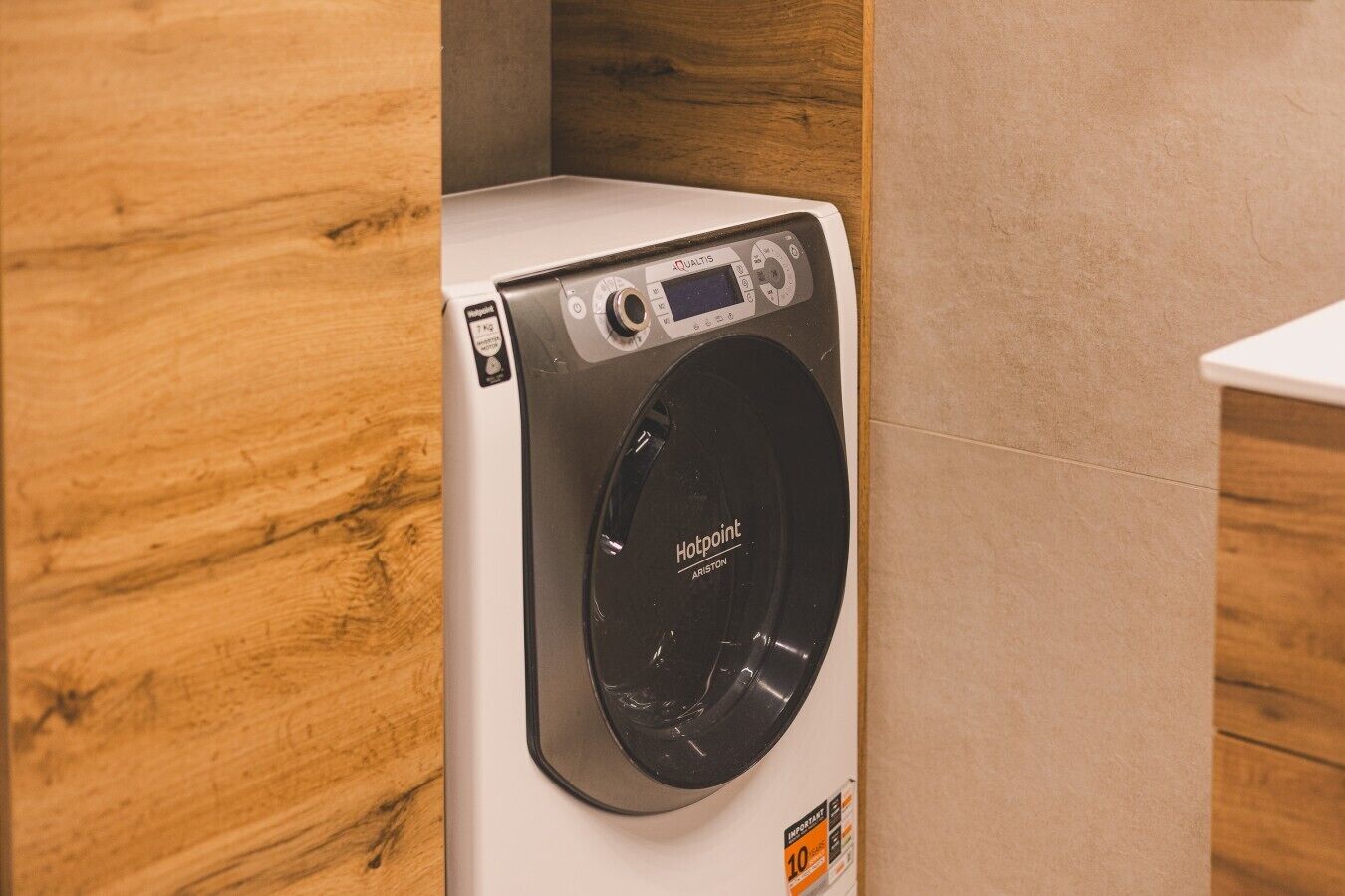 Lavadora de carga frontal con pantalla digital y panel de control, ubicada en un rincón con paneles de madera.