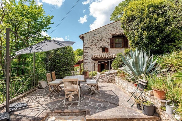 A stone patio with a table and chairs, surrounded by potted plants and a stone wall.