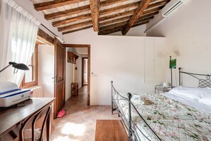 Un dormitorio con techo de madera, una cama con ropa de cama floral, un escritorio con impresora y una silla.