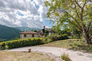 A rural house with a tiled roof, surrounded by greenery and hills.