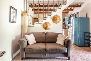Un salon moderne avec un canapé en cuir marron, un réfrigérateur bleu et un escalier dont les poutres en bois sont apparentes.